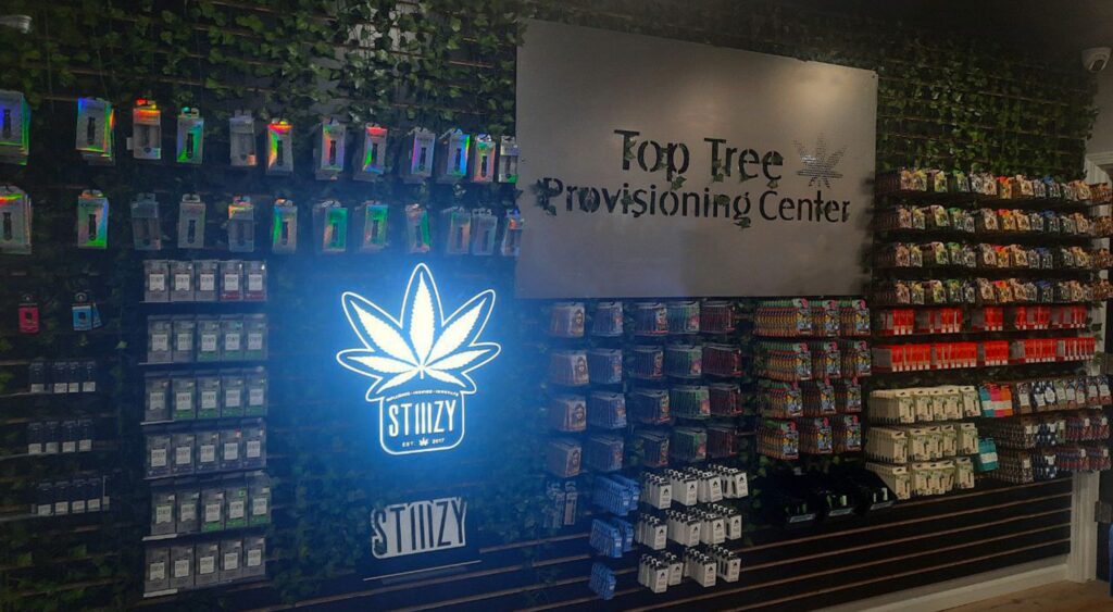 Wall display of diverse cannabis products at Top Tree Provisioning Center in Oscoda, Michigan, with a central carved metal sign featuring the company name.